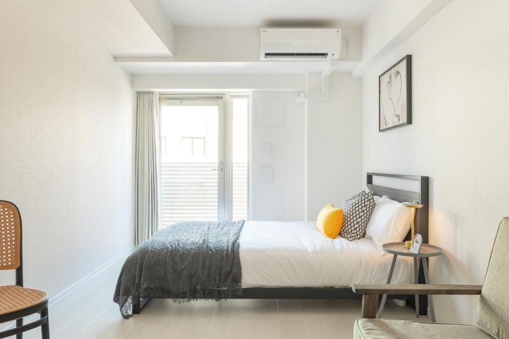A hotel room with a bed, a chair, a small table, and a window with blinds.