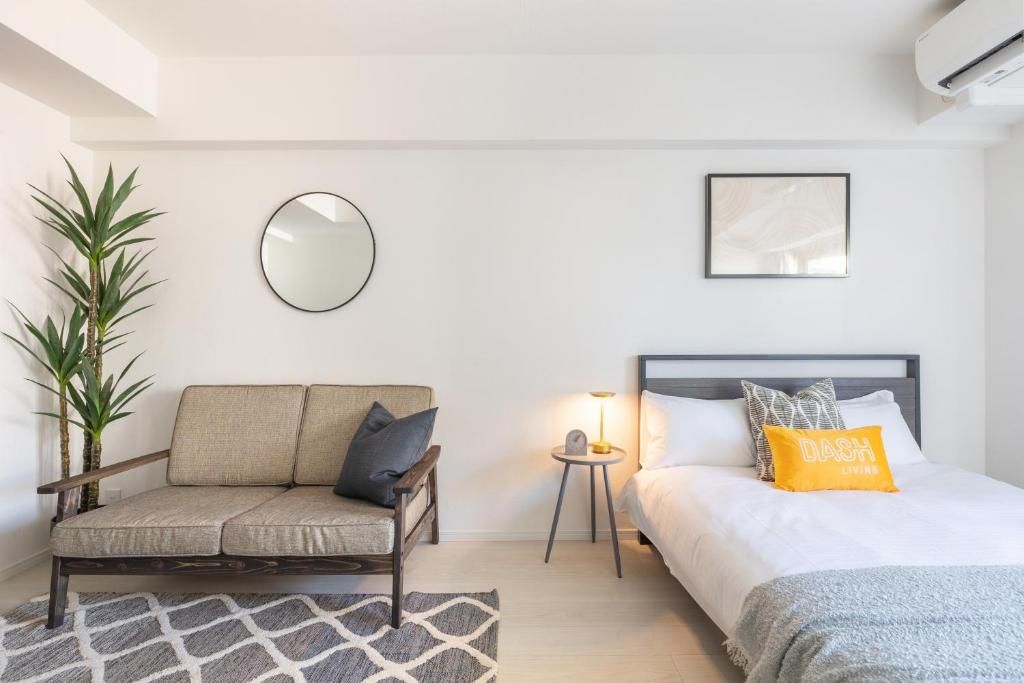 A bedroom with a bed, a sofa, a small table with a lamp, a mirror, and a potted plant.