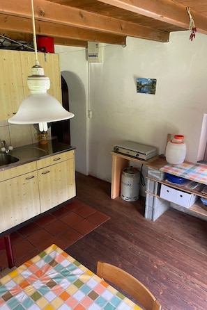 A small kitchen with wooden cabinets, a sink, a table with a colorful tablecloth, and a gas cylinder.