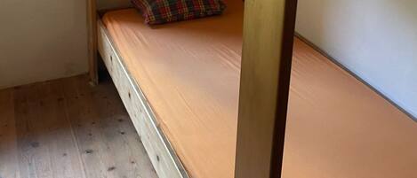 A bunk bed with a window above it, wooden flooring, and a small window on the left.