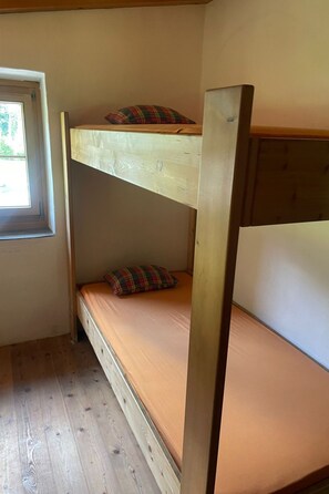 A bunk bed with a window above it, wooden flooring, and a small window on the left.