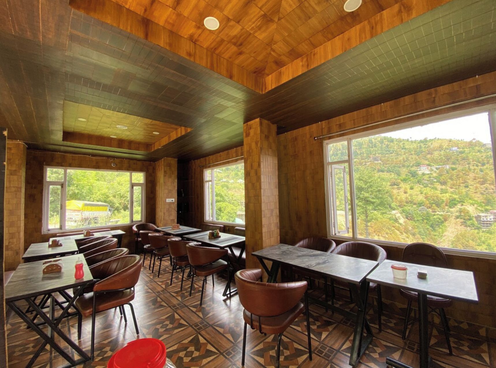 A dining area with tables and chairs, large windows, and a view of a green landscape.