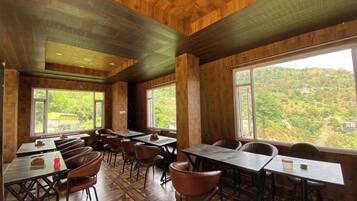 A dining area with tables and chairs, large windows, and a view of a green landscape.