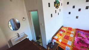 Un dormitorio con cama, mesita de noche, espejo, lavamanos y puerta que da a otra habitación.