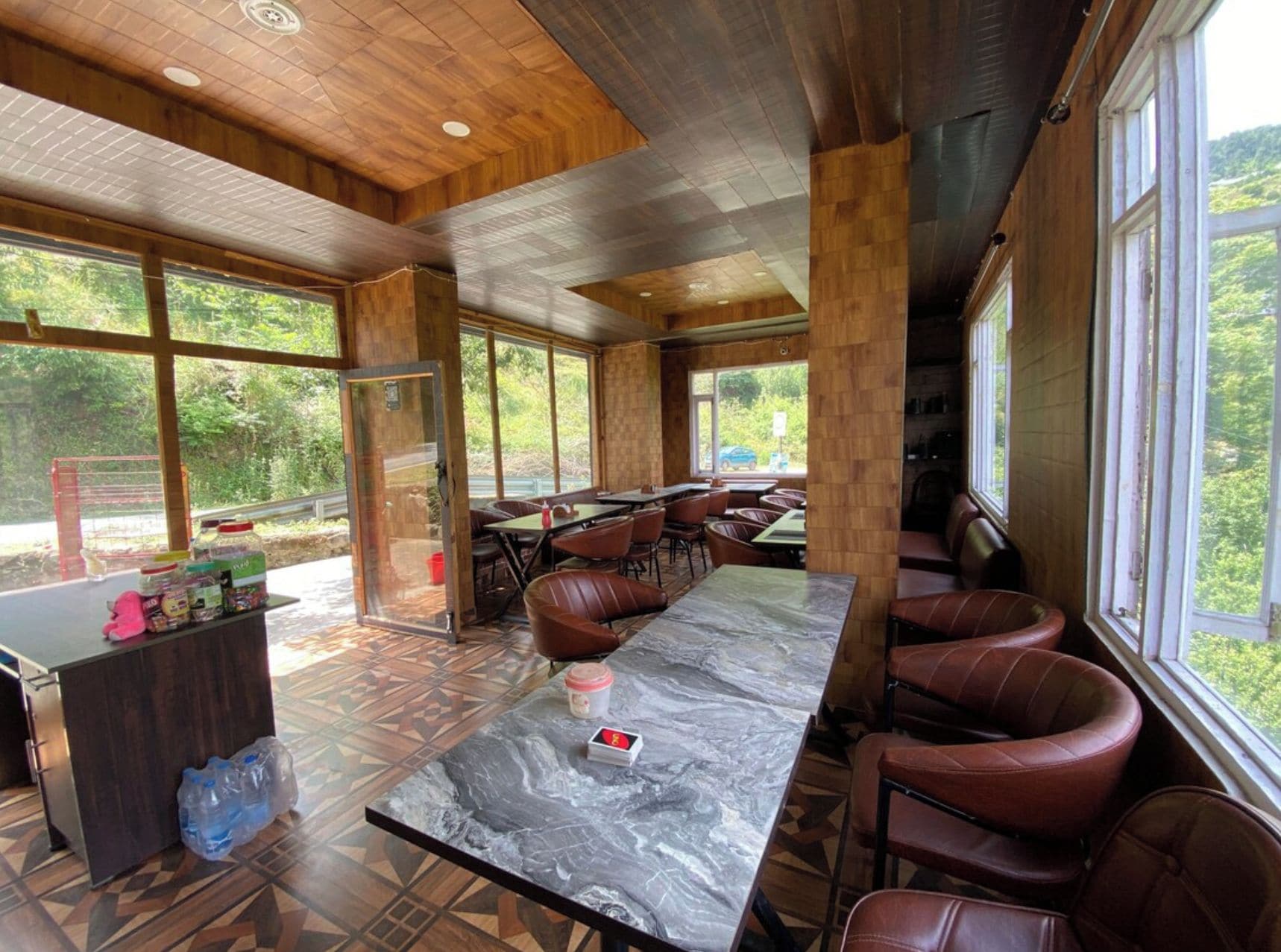 A spacious indoor area with a marble table, leather seating, and large windows offering a view of greenery.