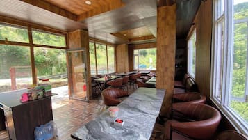 A spacious indoor area with a marble table, leather seating, and large windows offering a view of greenery.