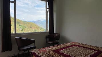 A room with a bed, two chairs, a window with a mountain view, and a patterned bedspread.
