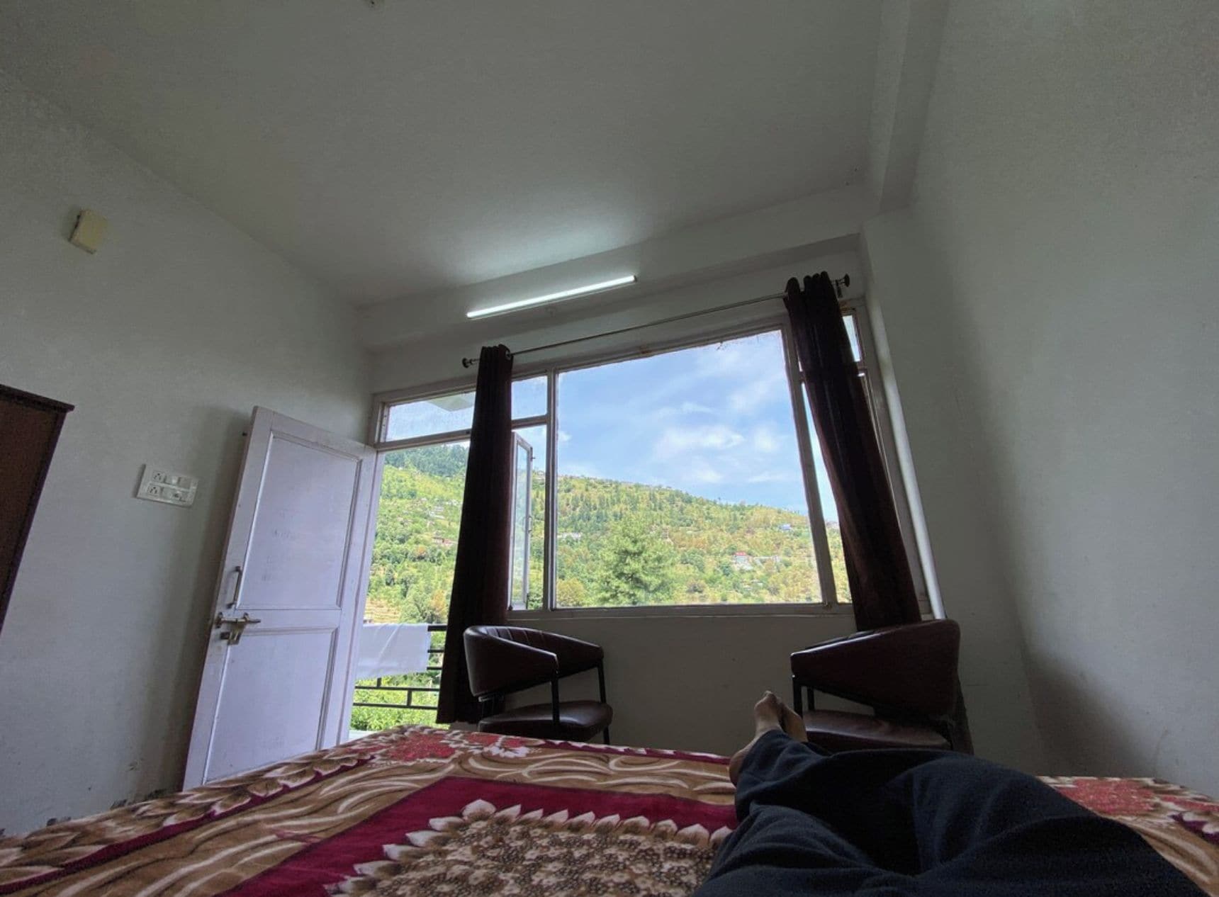A room with a bed, a window, a chair, and a door.