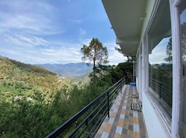 Un balcón con vista a un paisaje montañoso, una baranda y una ventana.
