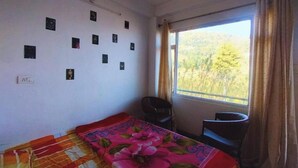 Una habitación con cama, una silla, un ventanal con vista a árboles y una pared decorada con pequeñas imágenes.