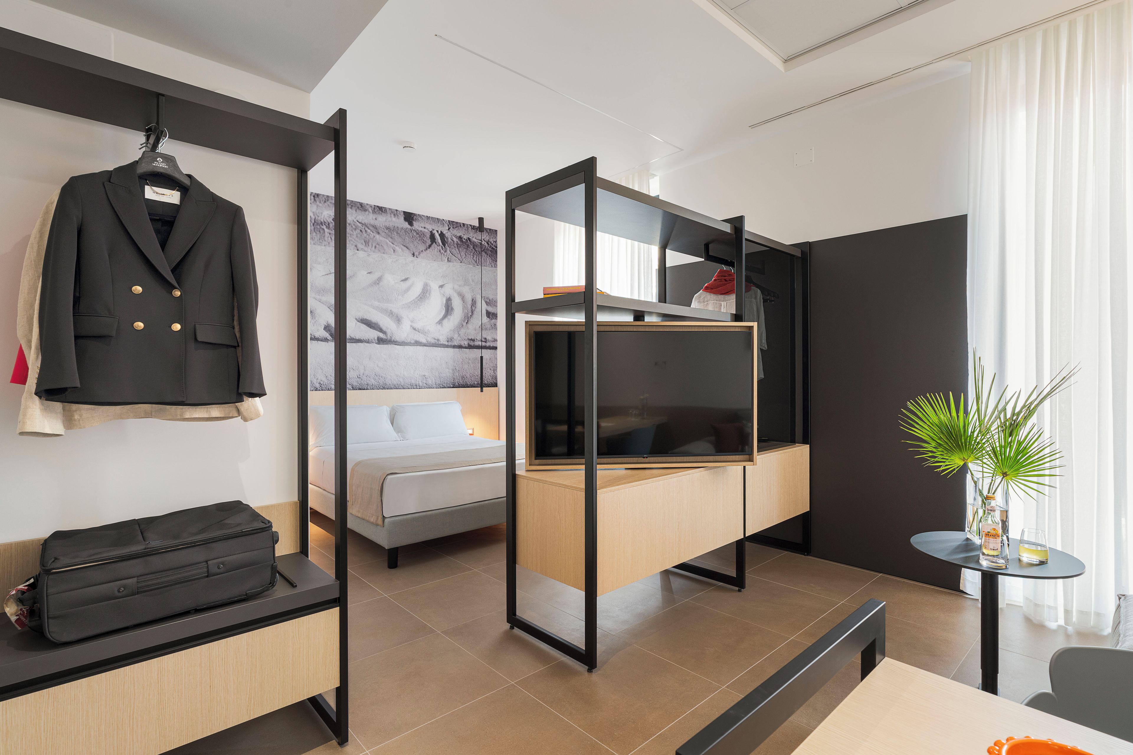 Una habitación de hotel moderna con cama, escritorio, armario y perchero.
