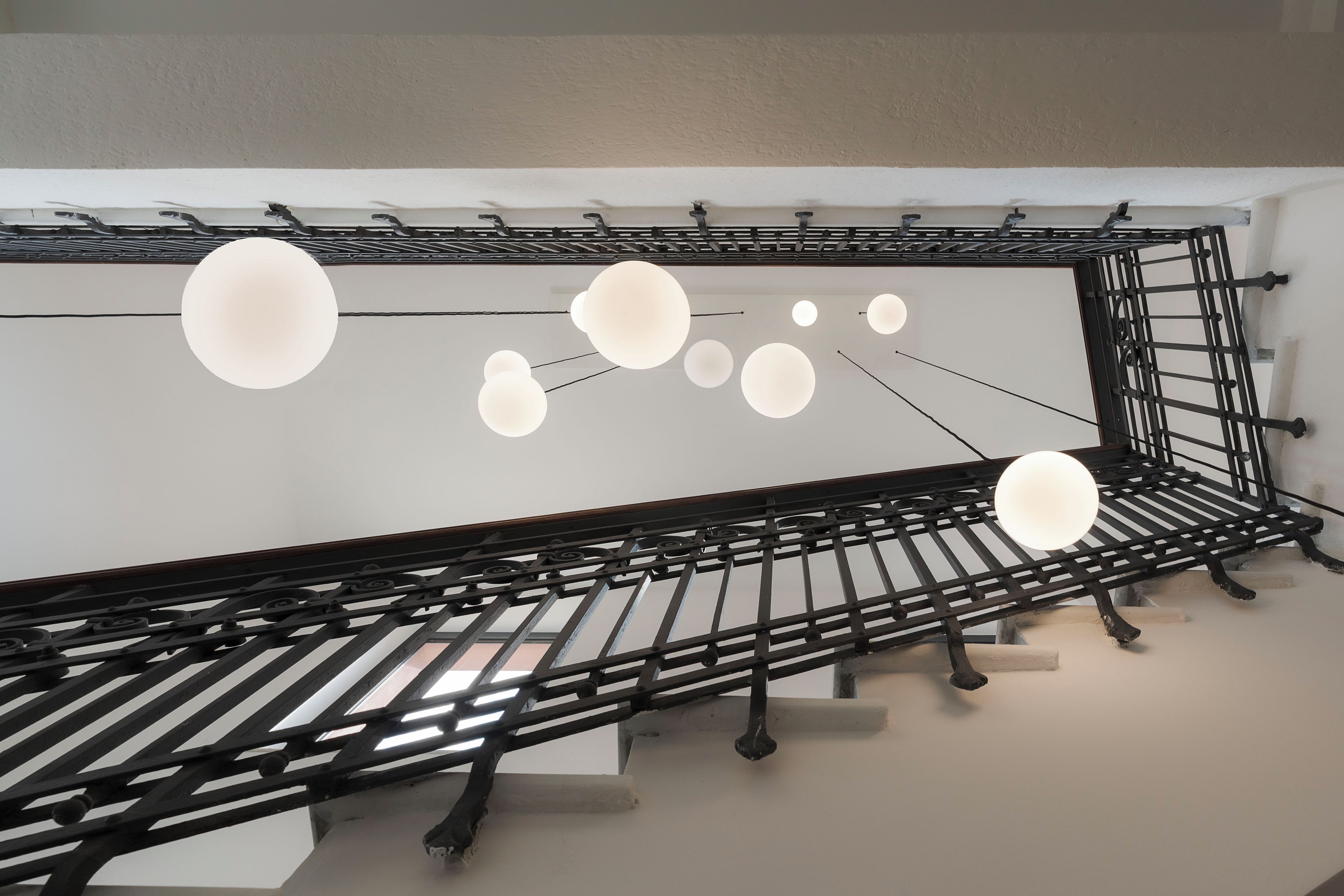 Ein modernes Interieur mit einer Metalltreppe und hängenden, kugelförmigen Leuchten.