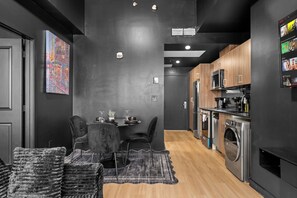 A modern kitchen with stainless steel appliances, a dining area with a table and chairs, and a black and white patterned rug. - Black Cave | Skyline Luxury 1BR • U/G Parking (Edmonton)