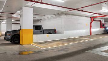 A parking garage with concrete pillars, a grey pickup truck, and red pipes.