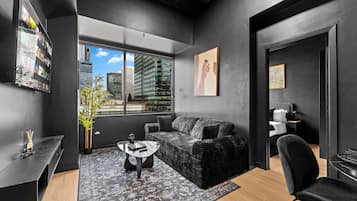 A modern living room with a sofa, a coffee table, a chair, and a large window offering a city view.