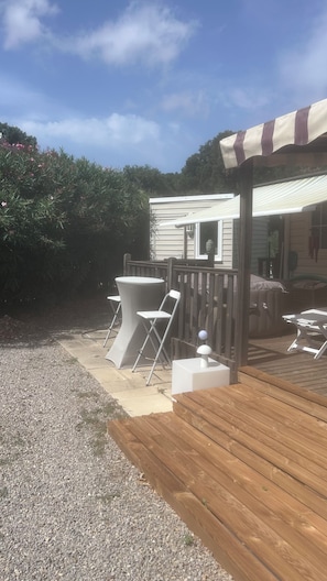 A wooden deck with outdoor furniture, a covered seating area, and a gravel path. - A gorgeous, fully equipped motorhome (Sainte-Maxime)