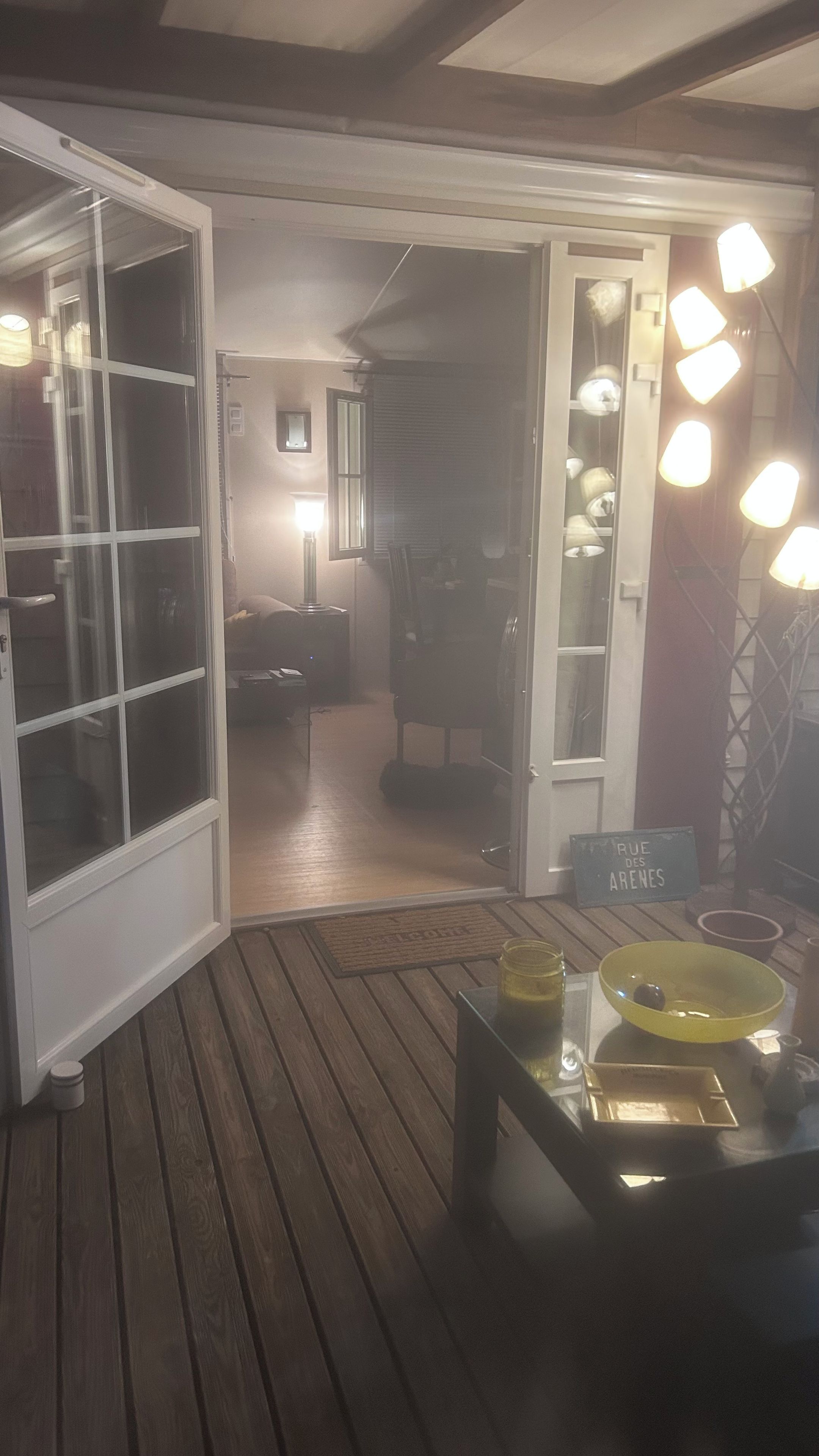 Un espacio interior con suelo de madera, un vidrio que da a otra habitación y una mesa con un cuenco amarillo y una placa.