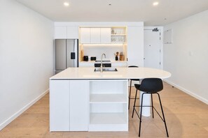A modern kitchen with a central island, white cabinetry, and a stainless steel refrigerator. - Wellington CBD 3BR with Pool, Gym & Views (Wellington)