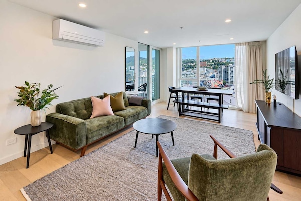 Spacious open-plan lounge at Alpha Street 1105 featuring a large TV, comfortable seating, modern décor, natural light and panoramic Wellington city views.