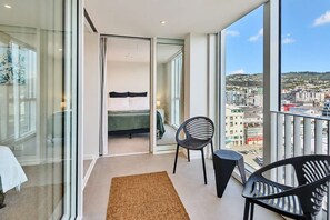 A balcony with a bed, two chairs, and a view of a cityscape. - Wellington CBD 3BR with Pool, Gym & Views (Wellington)