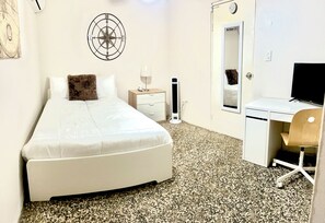 A hotel room with a bed, bedside table, lamp, desk, chair, and a wall-mounted compass. - Cozy Apt 1. Near the Beach, Airport, and More. All Set for a Hassle-Free Vacation (Carolina)