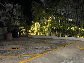 A nighttime outdoor area with potted plants and a paved surface marked with yellow lines. - Cozy Apt 1. Near the Beach, Airport, and More. All Set for a Hassle-Free Vacation (Carolina)