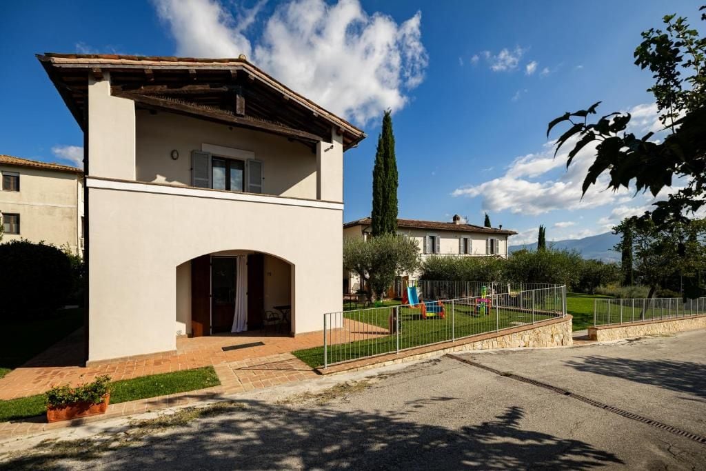 Un edificio a due piani con tetto piatto, un ingresso ad arco centrale e un cortile recintato con un'area giochi.