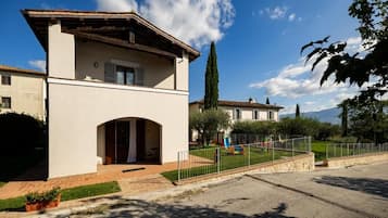 Un edificio a due piani con tetto piatto, un ingresso ad arco centrale e un cortile recintato con un'area giochi.