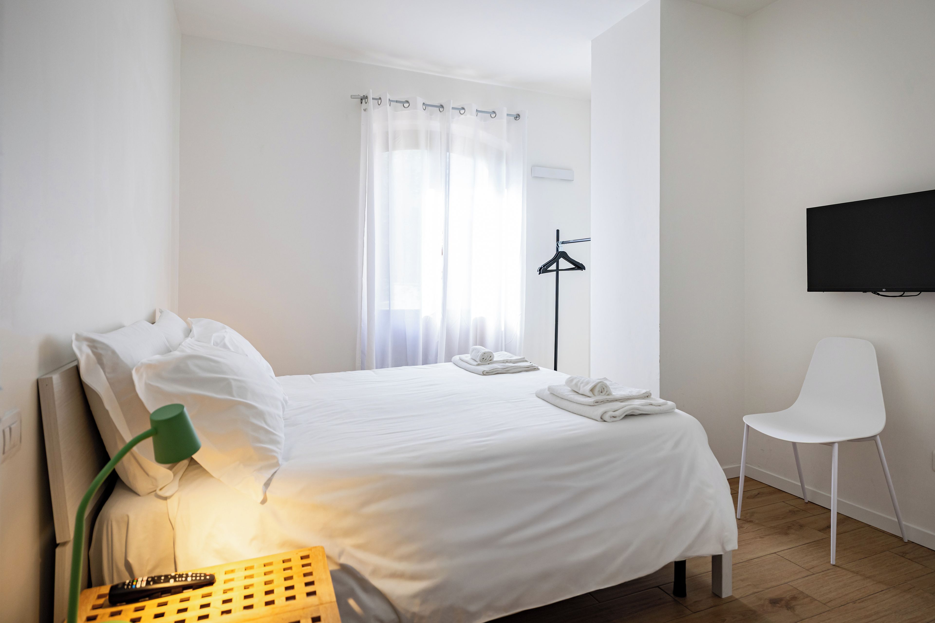Ein Hotelzimmer mit Bett, Sessel, Fernseher und einem Fenster mit Vorhängen.