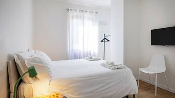 Ein Hotelzimmer mit Bett, Sessel, Fernseher und einem Fenster mit Vorhängen.