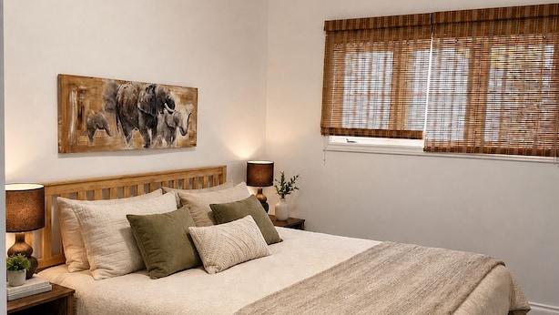 A bedroom with a wooden bed, a nightstand with a lamp, a wall-mounted painting, and a window with blinds. - Charming Chelsea Bungalow Central Location Modern Comforts (Chelsea)