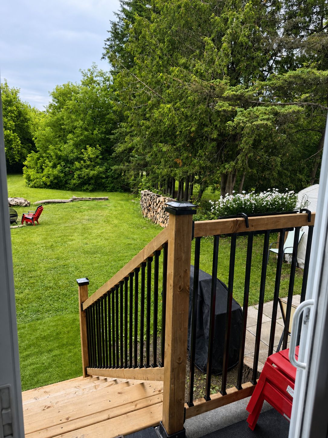 A wooden deck with a railing, a grill, and a lawn with chairs.