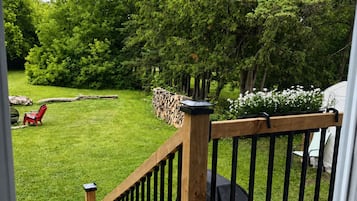 A wooden deck with a railing, a grill, and a lawn with chairs.