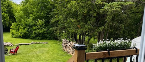Une terrasse en bois avec une rambarde, un barbecue et une pelouse avec des chaises.