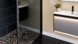 A modern bathroom with a glass shower enclosure, a white sink with a black faucet, and a mirror above the sink. - Charming Chelsea Bungalow Central Location Modern Comforts (Chelsea)
