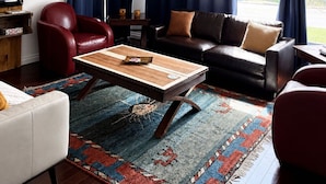 A living room with a leather sofa, a red armchair, a wooden coffee table, and a patterned rug. - Charming Chelsea Bungalow Central Location Modern Comforts (Chelsea)