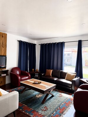Ein Wohnzimmer mit einem Ledersofa, einem roten Sessel, einem Holztisch und einem gemusterten Teppich.