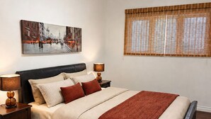 A bedroom with a bed, bedside tables, a painting, a window with blinds, and a rug. - Charming Chelsea Bungalow Central Location Modern Comforts (Chelsea)