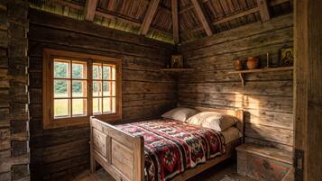 Une pièce rustique en bois, avec un lit, une fenêtre et des étagères ornées d’icônes religieuses.