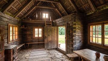 L’intérieur d’un chalet rustique, avec un sol en pierre, des murs en bois, une mezzanine et de grandes fenêtres.