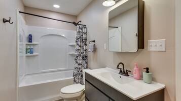 Une salle de bain équipée d’une baignoire, de toilettes, d’un meuble-lavabo avec un miroir et d’un rideau de douche.