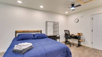 Une chambre à coucher comprenant un lit, un bureau, une chaise, un ventilateur de plafond et une horloge murale.