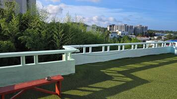 A grassy area with a white fence, a red bench, and buildings in the background.