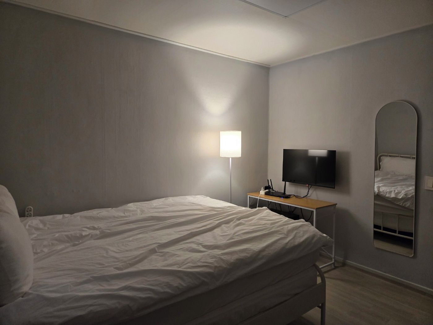 A hotel room with a bed, a flat-screen TV, a bedside table, a lamp, and a mirror.