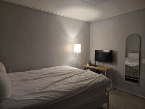 A hotel room with a bed, a flat-screen TV, a bedside table, a lamp, and a mirror. - Jiseulstay (Seogwipo)