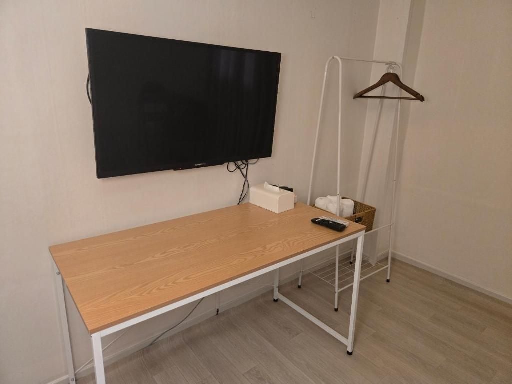 A room with a wooden desk, a mounted TV, a hanging clothes rack, and a white wall.