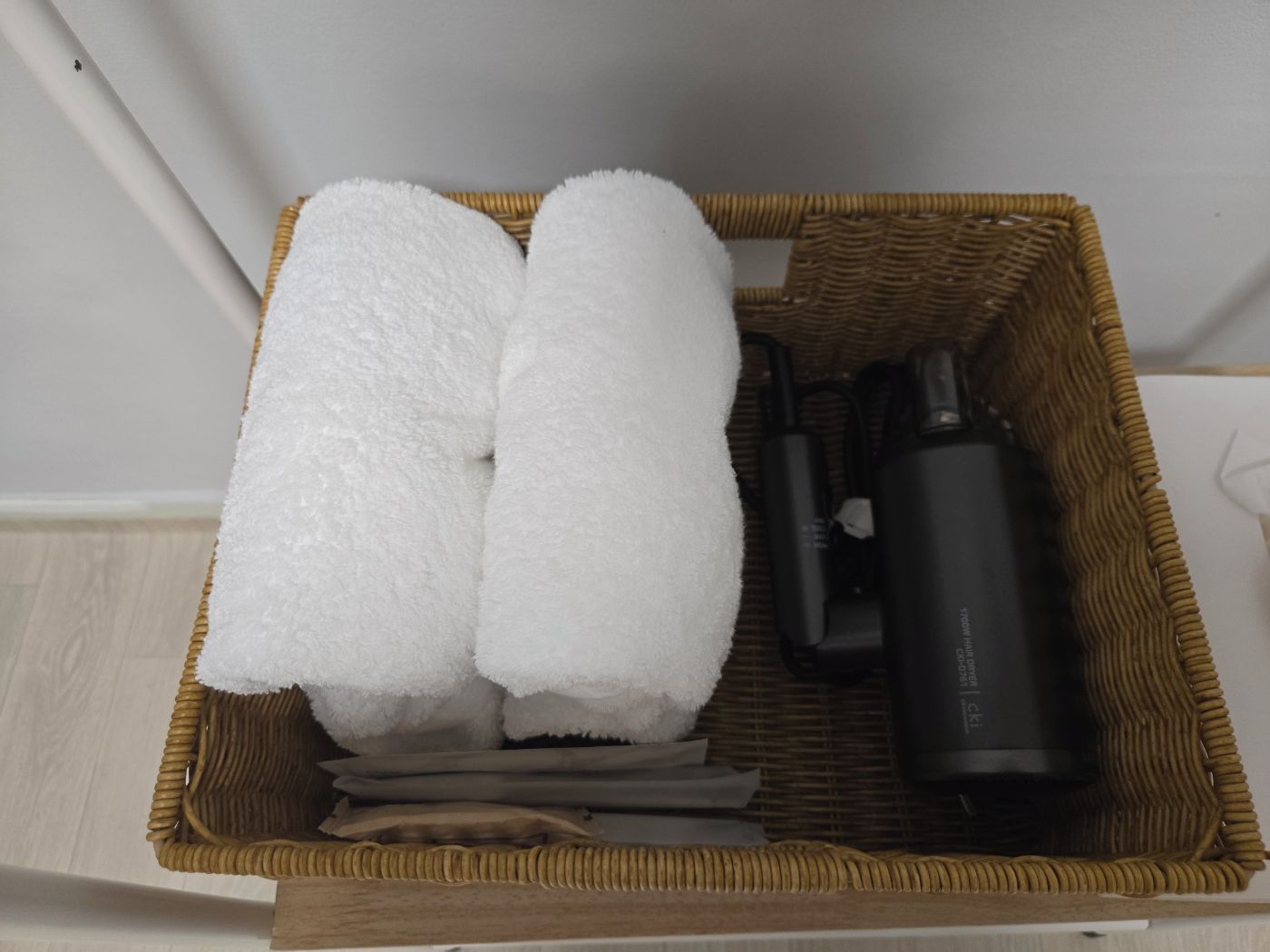 Uma cesta de vime com toalhas, uma garrafa preta e roupas dobradas.