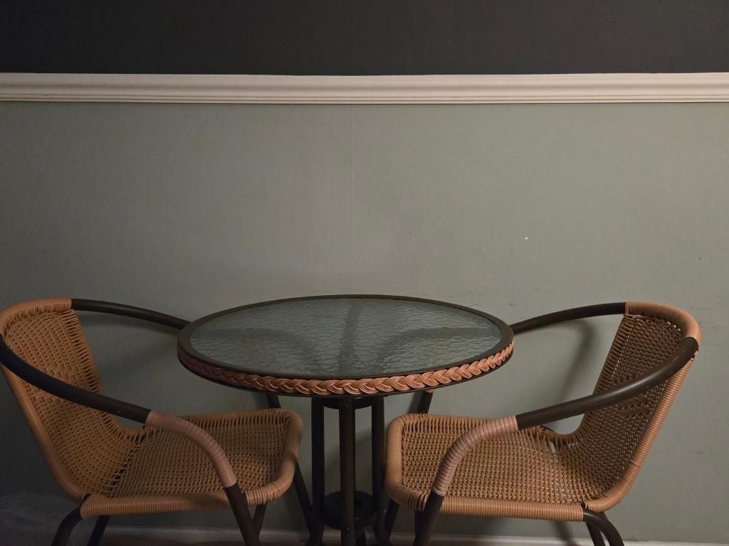 A round table with a glass top and two wicker chairs with metal frames.