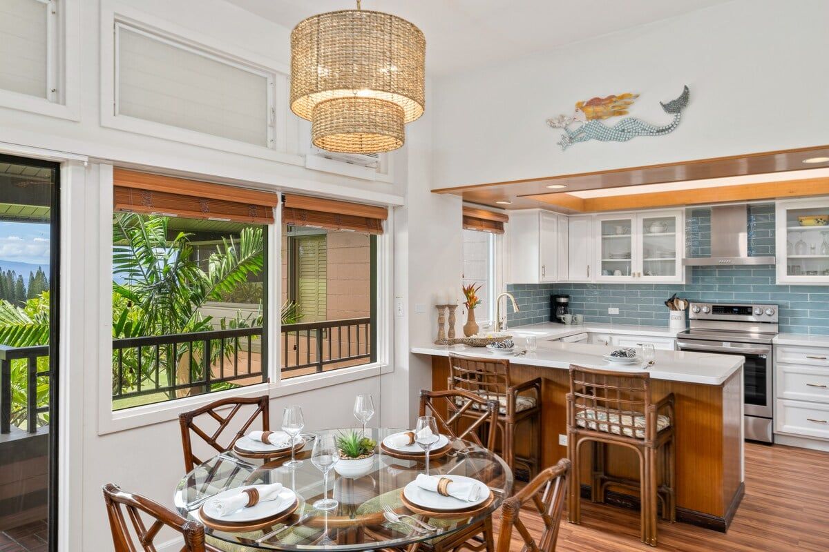 A modern kitchen with white cabinets, a stainless steel oven, and a dining area with a glass table and wicker chairs.