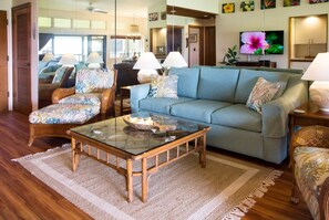 A living room with a sofa, two armchairs, a glass coffee table, and a television on the wall. - Ocean-view 1BR Kapalua condo with balcony, pool, AC, and full kitchen-Kapalua Ridge Villas 2521 (Lahaina)